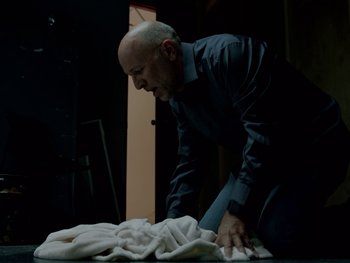 Movie still from “Casting JonBenet” (2017), directed by Kitty Green – A man kneeling down next to a pile of blankets; Medium shot, Low angle