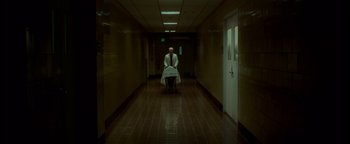 Movie still from “Casting JonBenet” (2017), directed by Kitty Green – A man sitting in a chair in a hospital hallway; Extreme Wide shot, Low angle