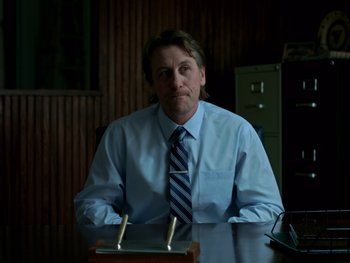 Movie still from “Casting JonBenet” (2017), directed by Kitty Green – A man sitting at a table in a room; Medium shot, Low angle