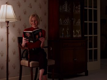 Movie still from “Casting JonBenet” (2017), directed by Kitty Green – A woman sitting in a chair reading a book; Medium shot, High angle