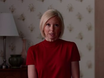 Movie still from “Casting JonBenet” (2017), directed by Kitty Green – A woman in a red shirt standing next to a lamp; Medium shot, Over the shoulder angle