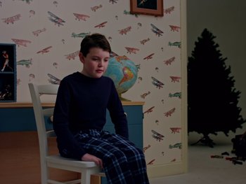 Movie still from “Casting JonBenet” (2017), directed by Kitty Green – A young boy sitting in a chair in a room; Medium shot, High angle