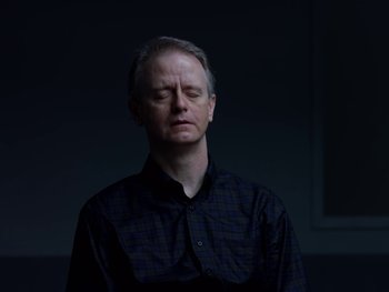 Movie still from “Casting JonBenet” (2017), directed by Kitty Green – A man in a black shirt is in a dark room; Close Up shot, Low angle