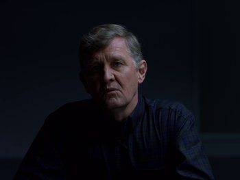 Movie still from “Casting JonBenet” (2017), directed by Kitty Green – A person sitting in a dark room; Close Up shot, Over the shoulder angle