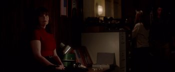 Movie still from “Casting JonBenet” (2017), directed by Kitty Green – A person standing next to a desk in a dark room; Medium shot, Over the shoulder angle