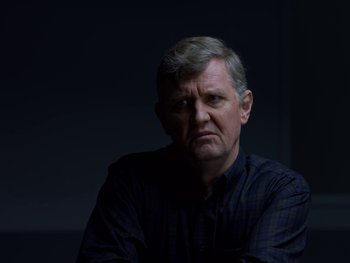 Movie still from “Casting JonBenet” (2017), directed by Kitty Green – An older man in a black shirt is looking at the camera; Close Up shot, Over the shoulder angle