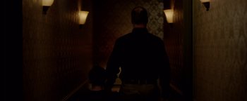 Movie still from “Casting JonBenet” (2017), directed by Kitty Green – A man standing in a dark hallway with a light on; Medium shot, Low angle