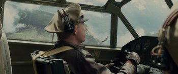 Movie still from “Unbroken” (2014), directed by Angelina Jolie – A man wearing a hat sitting in the cockpit of an airplane; Medium shot, Low angle