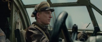 Movie still from “Unbroken” (2014), directed by Angelina Jolie – A man wearing a hat sitting in the driver's seat of an airplane; Close Up shot, Low angle