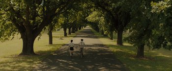 Movie still from “Unbroken” (2014), directed by Angelina Jolie – A man and a woman riding a bike down a tree lined street; Extreme Wide shot, High angle