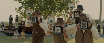 Movie still from “Unbroken” (2014), directed by Angelina Jolie – A group of men holding cameras in front of a tree; Wide shot, Low angle