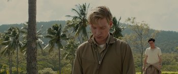 Movie still from “Unbroken” (2014), directed by Angelina Jolie – A young man standing in front of palm trees looking down; Close Up shot, Over the shoulder angle