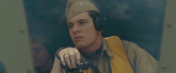 Movie still from “Unbroken” (2014), directed by Angelina Jolie – A man wearing a hat while holding a binocular; Close Up shot, High angle