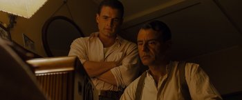 Movie still from “Unbroken” (2014), directed by Angelina Jolie – Two men standing next to each other with their arms crossed; Medium shot, Low angle