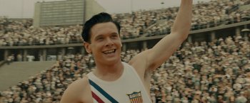Movie still from “Unbroken” (2014), directed by Angelina Jolie – A man is smiling and waving at the crowd; Close Up shot, High angle