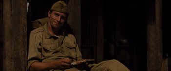 Movie still from “Unbroken” (2014), directed by Angelina Jolie – A man sitting on the ground holding a book; Medium shot, Over the shoulder angle