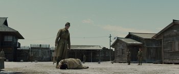 Movie still from “Unbroken” (2014), directed by Angelina Jolie – A man standing next to a man laying on the ground; Wide shot, Low angle