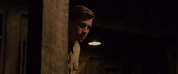 Movie still from “Unbroken” (2014), directed by Angelina Jolie – A man standing next to a wooden wall in a dark room; Medium shot, Low angle