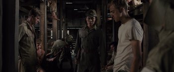 Movie still from “Unbroken” (2014), directed by Angelina Jolie – A man in a hat and uniform standing next to another man; Medium shot, Low angle