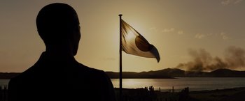 Movie still from “Unbroken” (2014), directed by Angelina Jolie – A person standing in front of a flag on a beach; Extreme Wide shot, Low angle