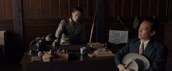 Movie still from “Unbroken” (2014), directed by Angelina Jolie – A man sitting at a table with a cup of coffee; Medium shot, Low angle