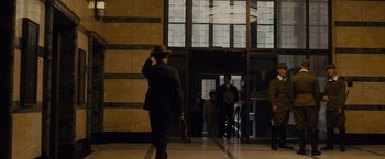 Movie still from “Unbroken” (2014), directed by Angelina Jolie – A man in a suit saluting in front of a building; Wide shot, Low angle