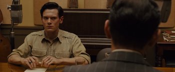 Movie still from “Unbroken” (2014), directed by Angelina Jolie – A man sitting at a table in front of another man holding a drink; Close Up shot, Over the shoulder angle
