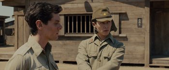 Movie still from “Unbroken” (2014), directed by Angelina Jolie – A man in a hat is talking to another man in a military uniform; Medium shot, Over the shoulder angle