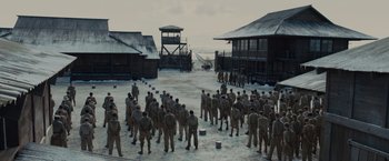 Movie still from “Unbroken” (2014), directed by Angelina Jolie – A group of men standing on top of a sandy beach; Extreme Wide shot, High angle