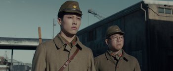 Movie still from “Unbroken” (2014), directed by Angelina Jolie – Two men in military fatigues are standing next to each other in front of a building; Medium shot, Low angle