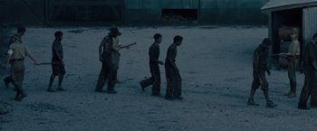 Movie still from “Unbroken” (2014), directed by Angelina Jolie – A group of men walking across a dirt field at night; Wide shot, High angle