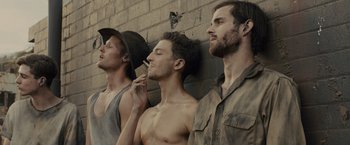 Movie still from “Unbroken” (2014), directed by Angelina Jolie – A group of men standing next to each other in front of a brick wall; Close Up shot, Low angle