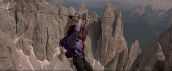 Movie still from “Cliffhanger” (1993), directed by Renny Harlin – A woman is holding onto a rope on the side of a mountain; Wide shot, Low angle