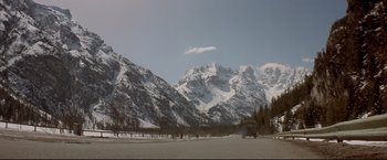 Movie still from “Cliffhanger” (1993), directed by Renny Harlin – A car driving down a road near a mountain range; Extreme Wide shot, Low angle