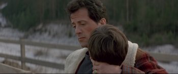 Movie still from “Cliffhanger” (1993), directed by Renny Harlin – A man and a boy are holding each other close together; Close Up shot, Over the shoulder angle