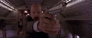 Movie still from “Cliffhanger” (1993), directed by Renny Harlin – A man in a suit and tie is holding a gun; Close Up shot, Low angle