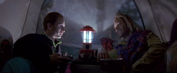 Movie still from “Cliffhanger” (1993), directed by Renny Harlin – Two people sitting at a table with a lantern; Medium shot, Low angle