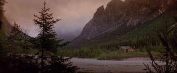 Movie still from “Cliffhanger” (1993), directed by Renny Harlin – A house sitting on the side of a river in front of a mountain range; Extreme Wide shot, High angle