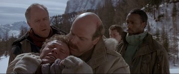 Movie still from “Cliffhanger” (1993), directed by Renny Harlin – A man with a bald head is holding a woman; Close Up shot, Over the shoulder angle