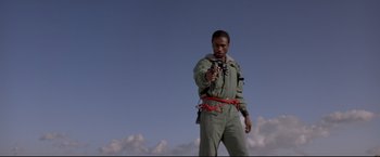 Movie still from “Cliffhanger” (1993), directed by Renny Harlin – A man standing in the middle of a field holding a gun; Medium shot, Low angle