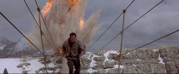 Movie still from “Cliffhanger” (1993), directed by Renny Harlin – A man running across a bridge with a bunch of smoke coming out of it; Wide shot, Low angle