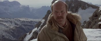 Movie still from “Cliffhanger” (1993), directed by Renny Harlin – A man with a beard is standing on top of a mountain; Close Up shot, Low angle