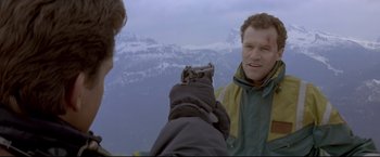 Movie still from “Cliffhanger” (1993), directed by Renny Harlin – A man holding a gun pointed at another man; Medium shot, Over the shoulder angle