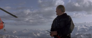 Movie still from “Cliffhanger” (1993), directed by Renny Harlin – A man standing on top of a mountain holding a cell phone; Medium shot, Low angle