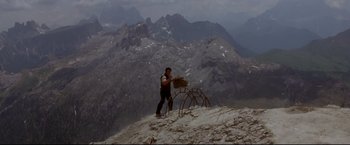 Movie still from “Cliffhanger” (1993), directed by Renny Harlin – A man standing on top of a mountain near a chair; Wide shot, Low angle