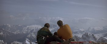 Movie still from “Cliffhanger” (1993), directed by Renny Harlin – Two men sitting on top of a hill with a mountain in the background; Extreme Wide shot, Low angle