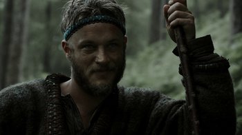 Movie still from “Vikings” (2013), created by Michael Hirst – A person holding a stick in a forest; Close Up shot, Low angle