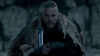 Movie still from “Vikings” (2013), created by Michael Hirst – A man with a beard holding a large sword; Close Up shot, Low angle