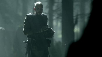 Movie still from “Vikings” (2013), created by Michael Hirst – A man holding a cat while standing in the woods; Medium shot, Low angle
