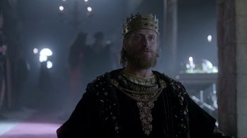 Movie still from “Vikings” (2013), created by Michael Hirst – A man wearing a crown standing in a dark room; Medium shot, Low angle